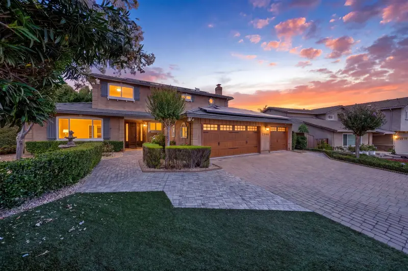 Two-story stucco home with wood garage doors and a paver driveway at twilight, Milpitas