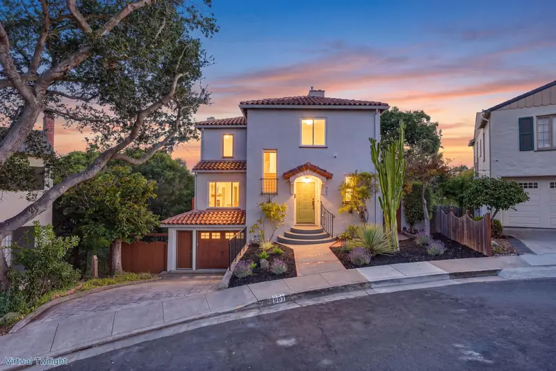 Spanish-style stucco home with a tile roof and a lit entry at twilight, Oakland