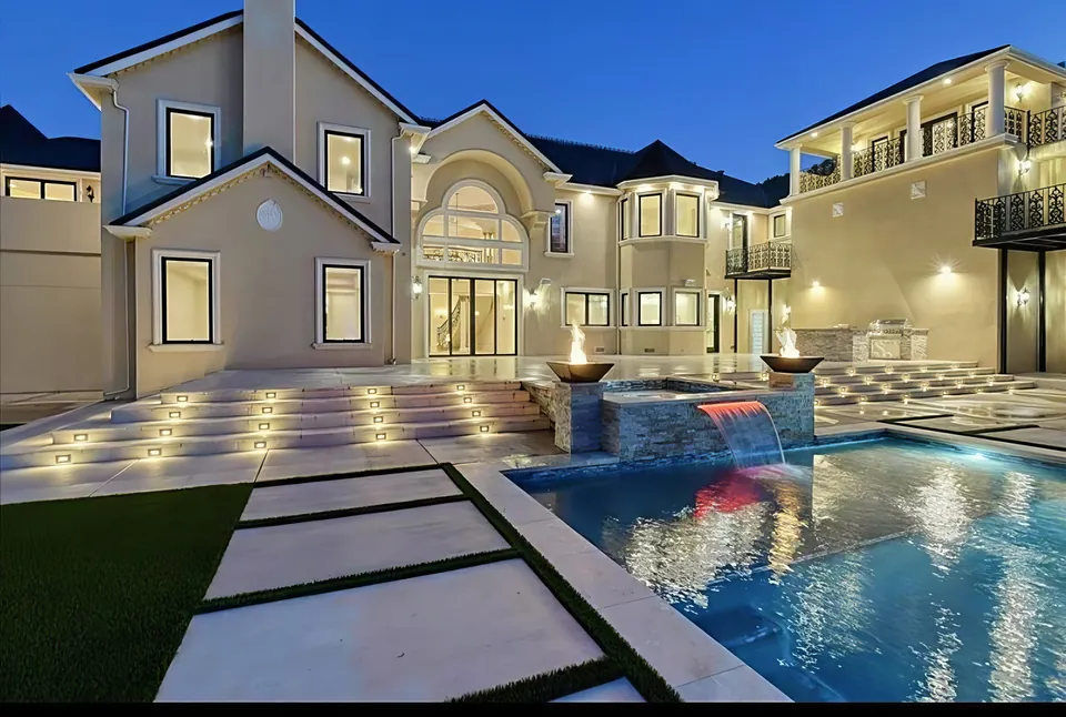 Estate pool and spa: stacked-stone spa spillway below a lit two-story home
