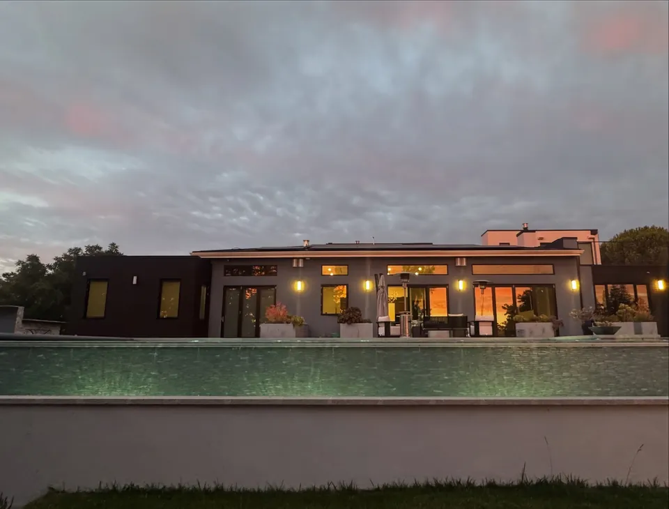 Raised vanishing-edge pool wall in front of a modern home with lit windows at golden hour